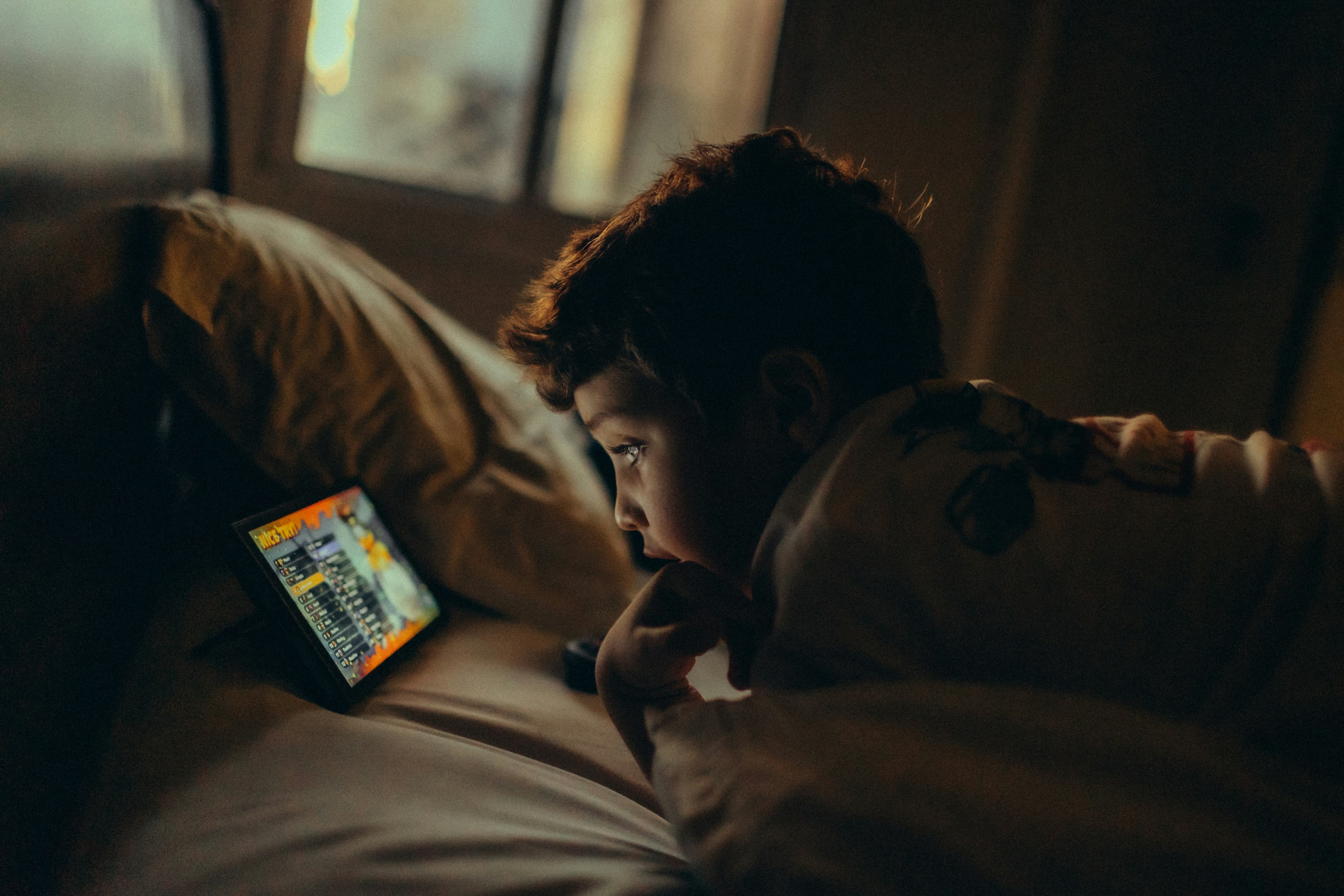 暗い部屋でタブレットを見る子ども