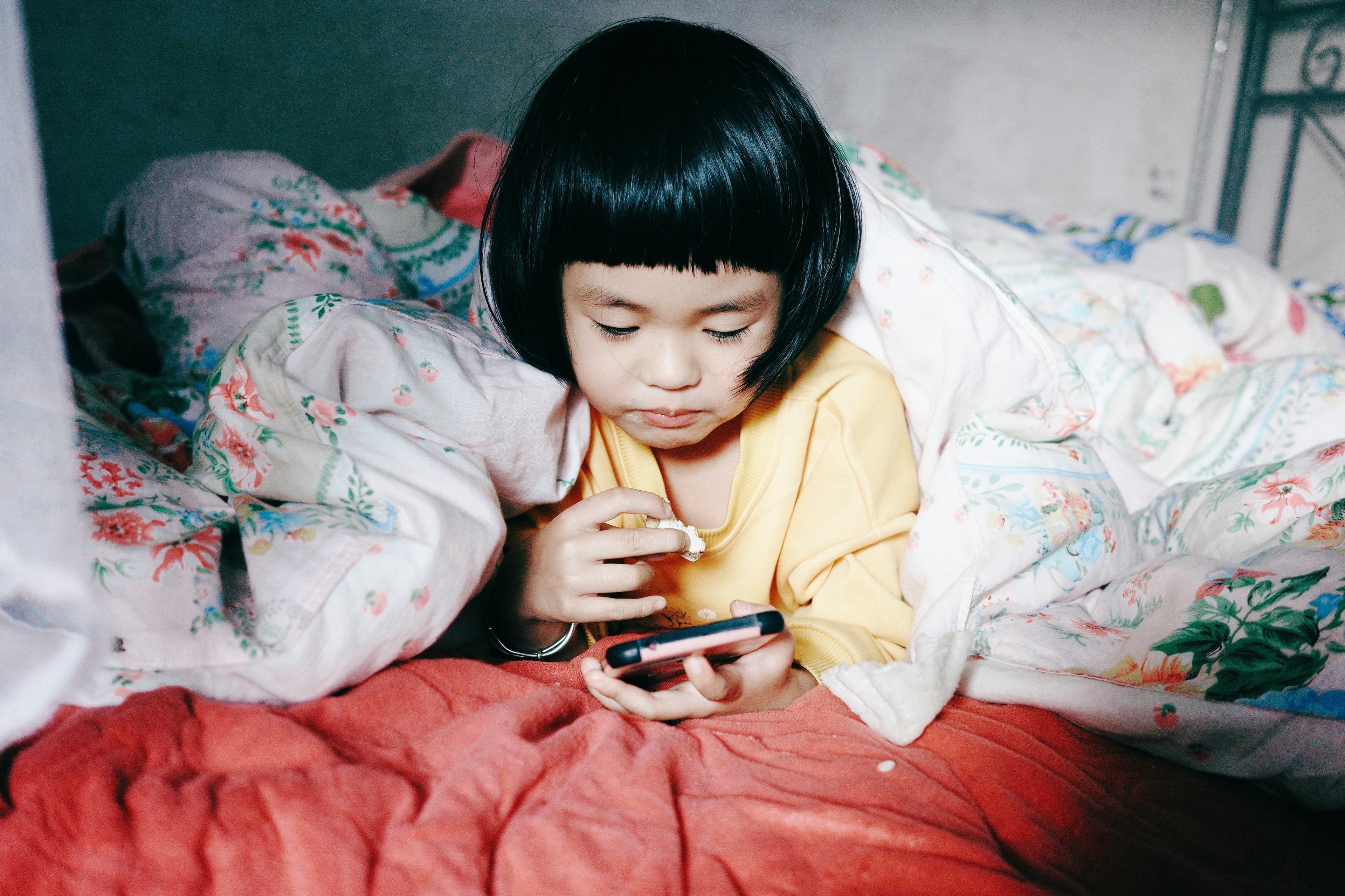 布団の中でスマホを見るアジア系の子ども